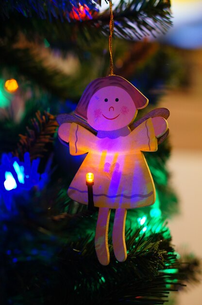 Wooden Christmas tree angel ornament hanging on a tree with a lit Christmas light