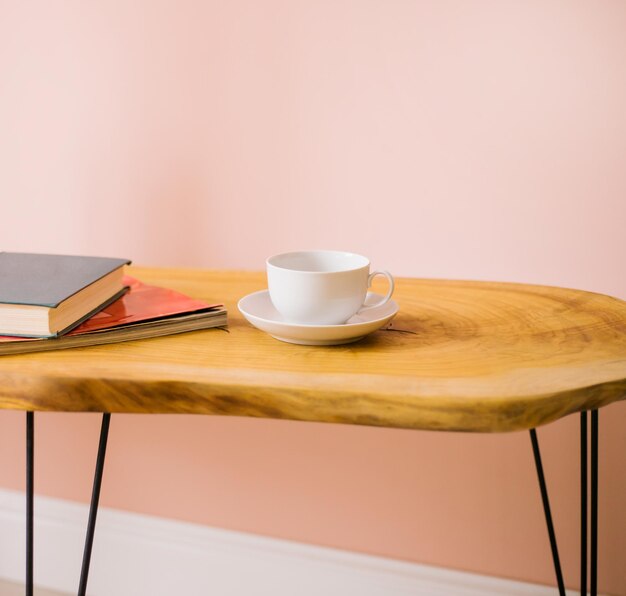 Деревянный журнальный столик. на столе и книгах чашка с блюдцем. современный интерьер. комфорт и уют.