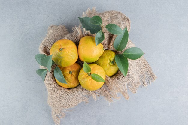 Wooden crate covered with a piece of cloth, filled with tangerines on marble . 