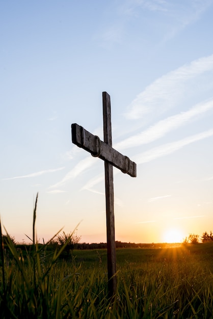 Wooden cross in a grassy field with the sun shining in a blue sky