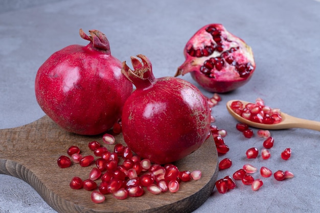 A wooden cutting board full of pomegranate on blue surface.