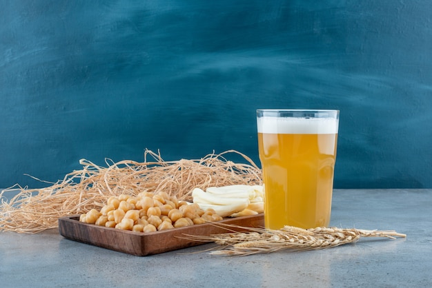 A wooden cutting board of peas and cheese with glass of beer. High quality photo