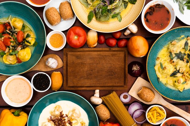 Wooden cutting board surrounded by pasta dishes and ingredient on table