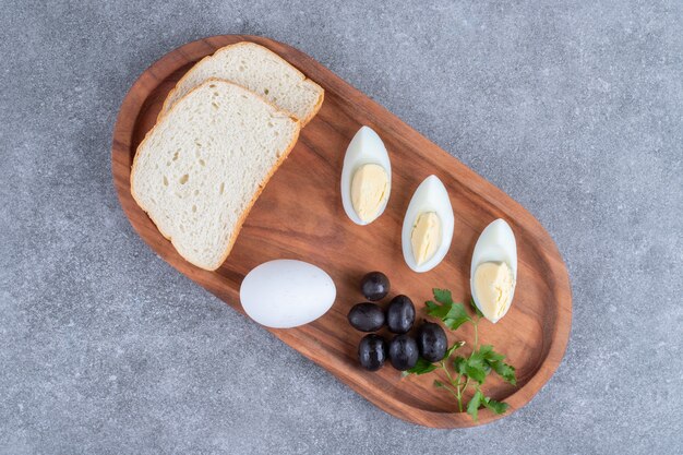 Деревянная разделочная доска с вареным яйцом и кусочками хлеба. Фото высокого качества