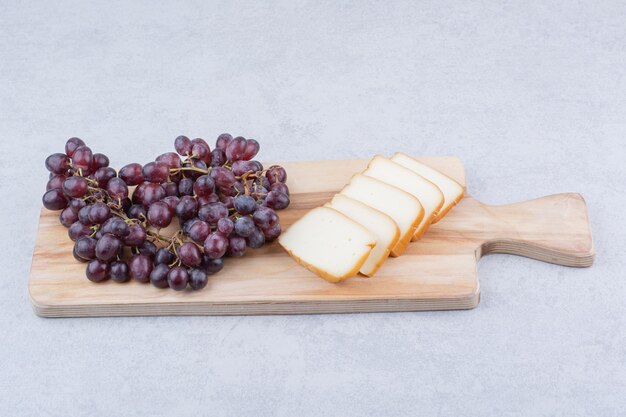 Деревянная разделочная доска с нарезанным хлебом и виноградом. Фото высокого качества
