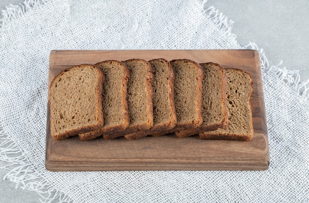 A wooden cutting board with slices of brown bread .