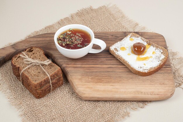 A wooden cutting board with toast and cup of tea on sackcloth .