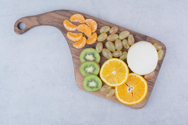 A wooden cutting board with whole cheese and sliced fruits.