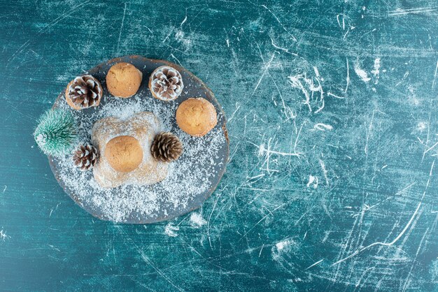 A wooden dark board with cupcakes and pinecones powdered with sugar.