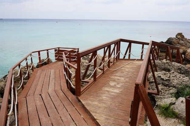 Wooden deck on the shore surrounded by rocks and sea under a cloudy sky