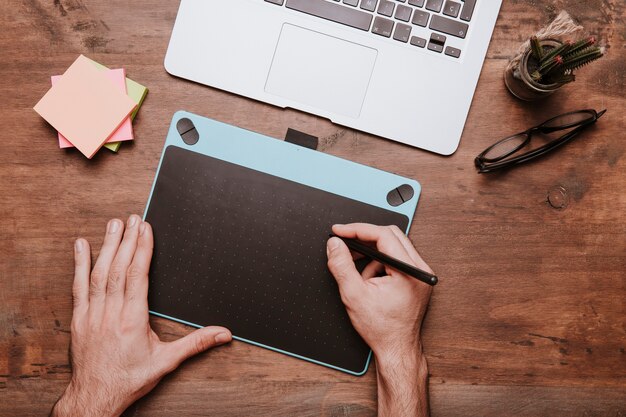 Free photo wooden desk concept with hands drawing on design tablet