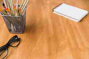 Free photo wooden desk with glasess, pencils and notebook