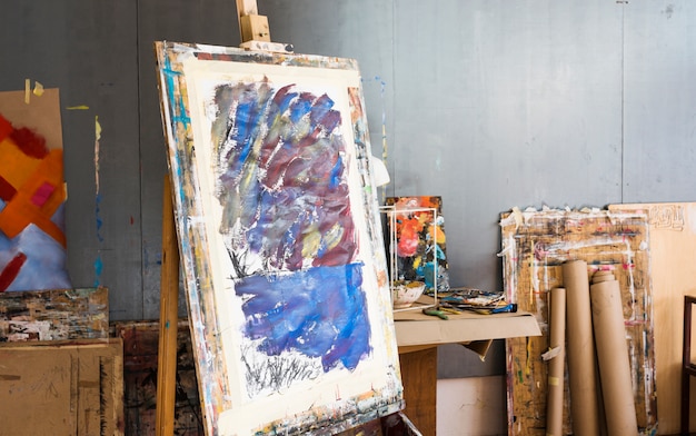 Free photo wooden easel with messy painting in artist's workshop