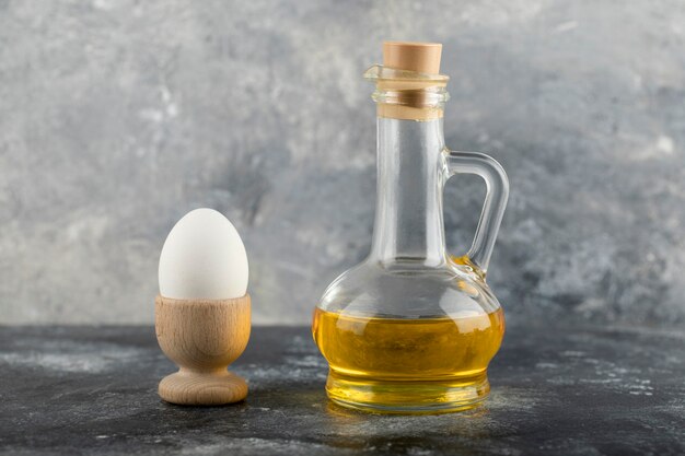 A wooden eggcup with boiled chicken egg and a glass bottle of oil. 