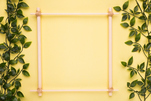 Free photo wooden empty frame on yellow paper with green artificial leaves