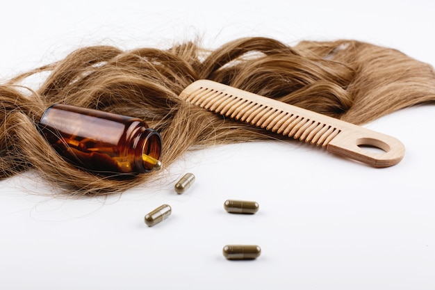 Wooden hair comb and bottle with vitamins lie on brown hair curls