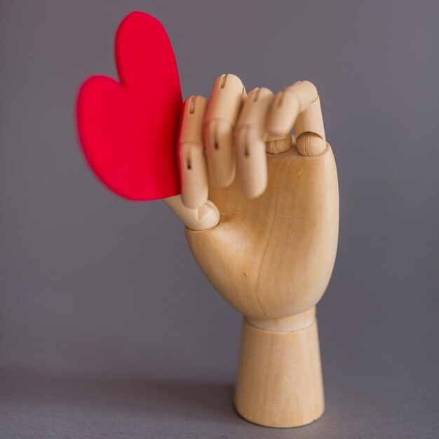 Wooden hand holding red heart on table 