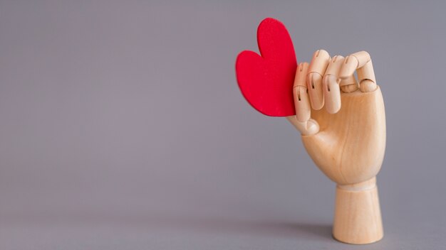Wooden hand holding red heart 