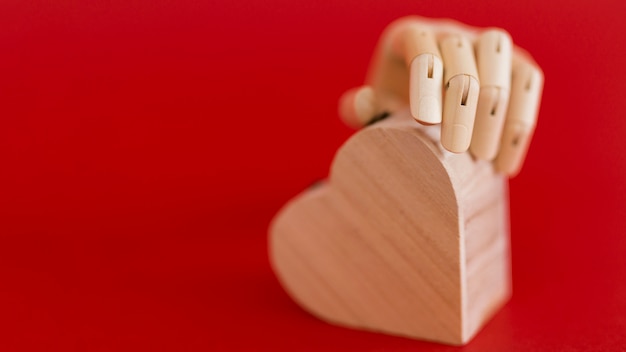 Wooden hand holding wooden heart on red table