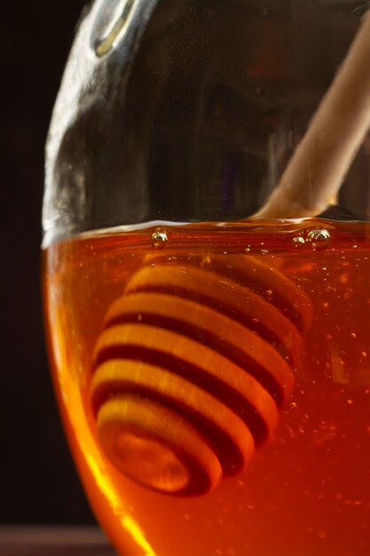 Wooden honey dipper in transparent jar of honey