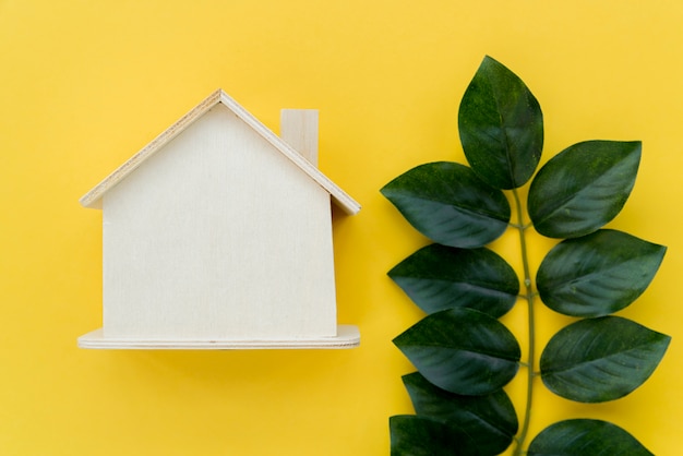 Wooden house model near the green leaves against yellow background