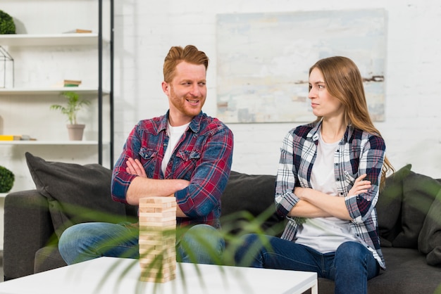 Wooden jenga in front of young couple with arm crossed looking at each other