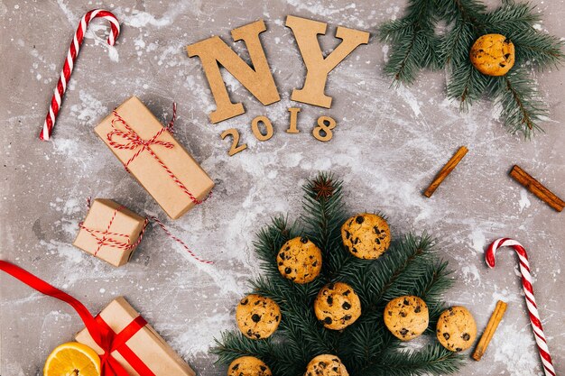 Wooden letters 'NY 2018' lie in the floor surrounded with cookies, fir branches, red white candies and present boxes