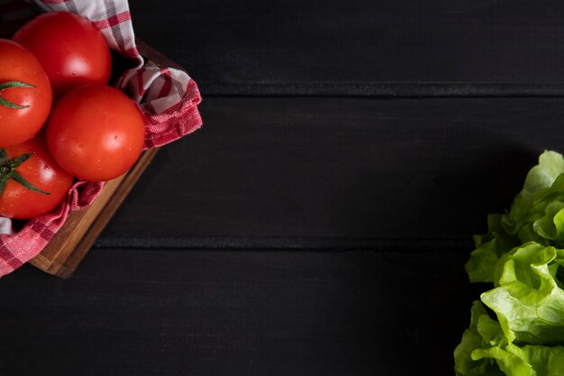 A wooden old box full of fresh red juicy tomatoes with lettuce salad . High quality photo