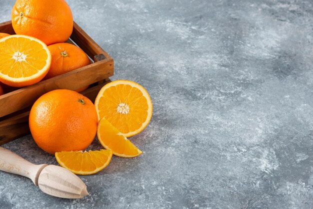 Деревянная старая коробка, полная сочных апельсиновых фруктов на каменном столе.