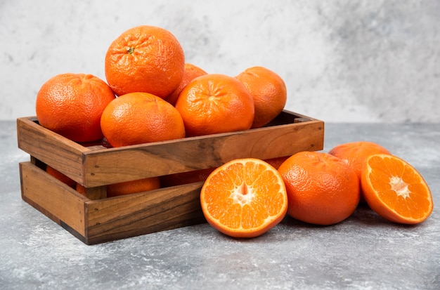 A wooden old box full of juicy orange fruit on stone table .