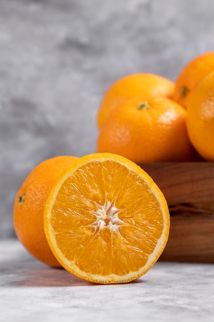 A wooden old box full of whole and sliced orange fruits placed on marble