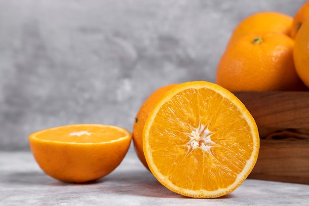 A wooden old box full of whole and sliced orange fruits placed on marble