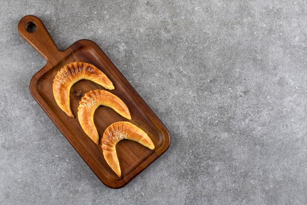 Wooden pate of three delicious crescent shaped vanilla cookies on marble.