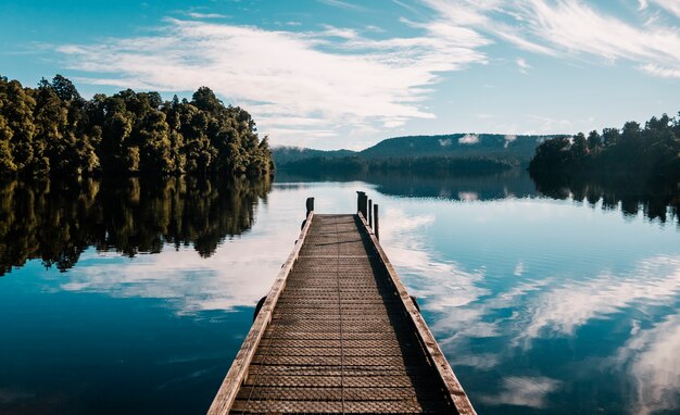 Wooden pathway with trees and a blue sky reflected on Lake Mapourika Waiho in New Zealand