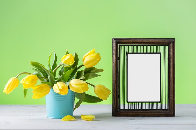 A wooden photo frame near yellow tulips on a wooden surface
