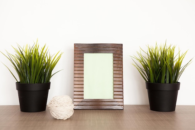 Wooden photo frame next to two pots with grass over a white background wall
