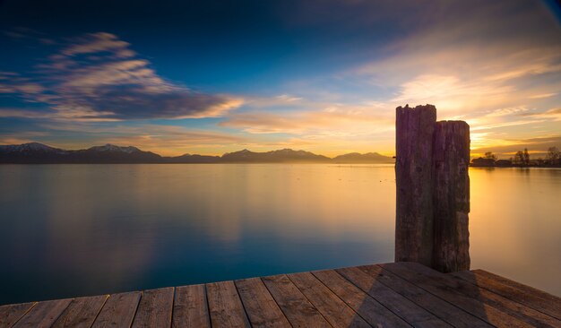 山脈と日の出のある穏やかな海の上の木製の桟橋