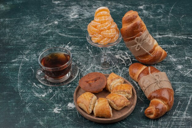 Wooden plate of bakery with croissant and tangerine .