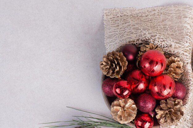 Деревянная тарелка из красных новогодних шаров и шишек на мешковине.