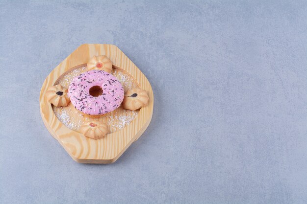 A wooden plate of delicious pink doughnut with sweet cookie. 