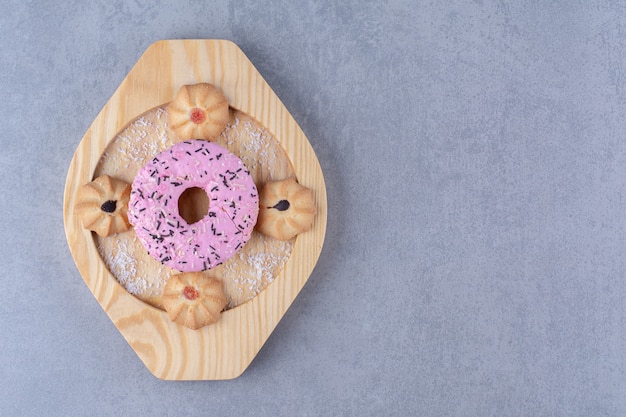 A wooden plate of delicious pink doughnut with sweet cookie.
