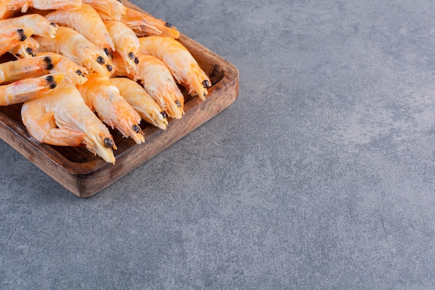 Free photo a wooden plate of delicious shrimps on a stone surface