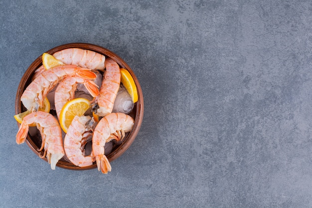 Free photo a wooden plate of delicious shrimps with ice cubes and sliced lemon on a stone surface
