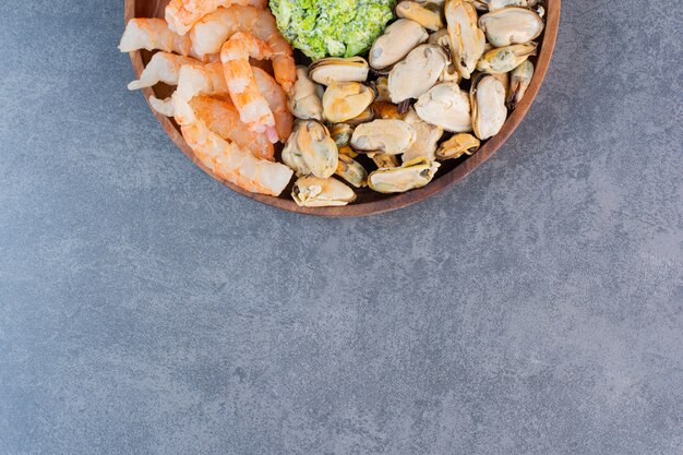 A wooden plate of delicious shrimps with tasty crab sticks on a stone surface 