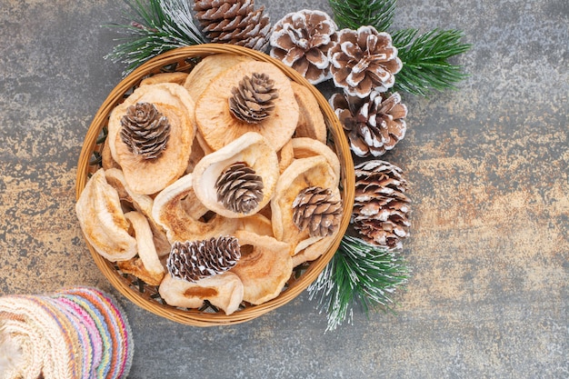 Wooden plate of dried apple rings and pinecones on stone.