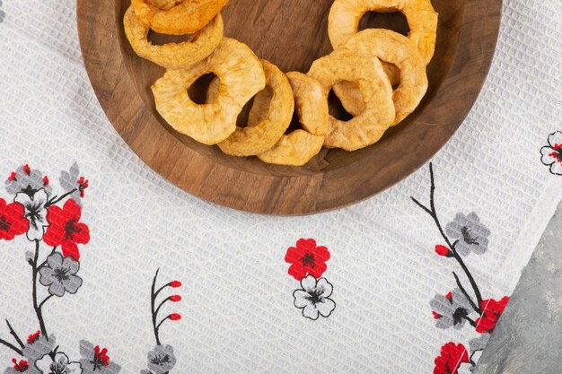 Wooden plate of dried apple rings placed on white tablecloth. 