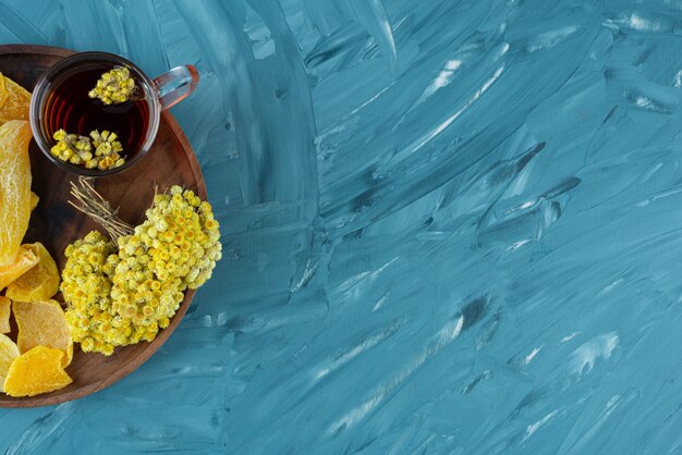 Деревянная тарелка сухофруктов и стакан чая на синем фоне.