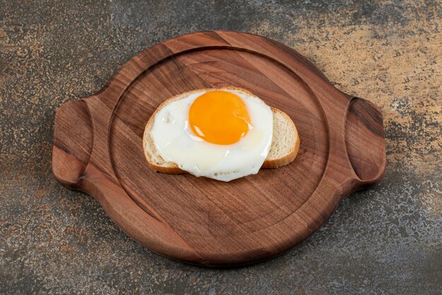 A wooden plate of egg on the white bread slice.