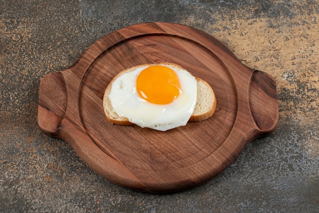 A wooden plate of egg on the white bread slice.