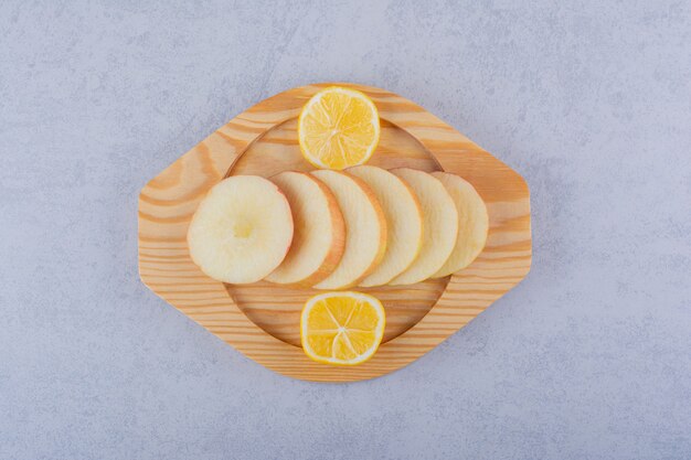 Wooden plate of fresh apple slices and lemon on stone.